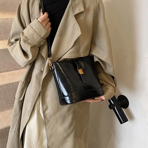 Sac seau noir brillant avec détails dorés et bandoulière sur manteau kaki