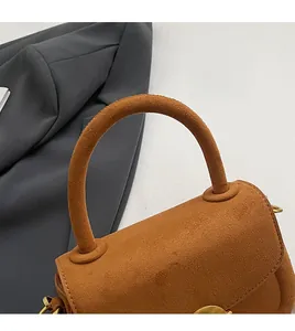 Detail of curved suede top handle and golden metal hardware on a brown handbag
