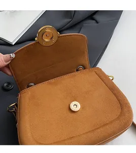 Close-up of brown suede saddle bag featuring a vintage gold magnetic clasp and texture