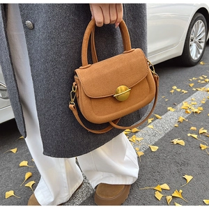 Close-up of brown suede saddle bag with golden buckle on a street with yellow ginkgo leaves