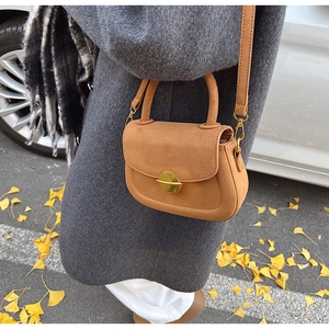 Close-up of brown suede saddle bag with golden metal buckle and crossbody strap detail