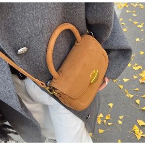 Brown suede leather bag with gold oval clasp held against a grey coat in autumn setting