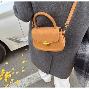 Close-up of a camel suede saddle bag with gold metal buckle against autumn leaves