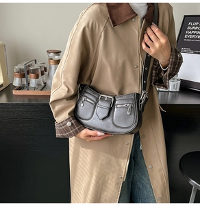Detail of a black half-moon crossbody bag with zippers and retro buckle on a model