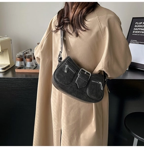 Detail einer schwarzen Wildleder-Umhängetasche mit Taschen über einem beigen Trenchcoat