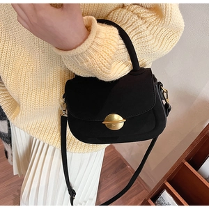 Detail of a vintage black crossbody saddle bag with gold clasp on a cozy knit outfit
