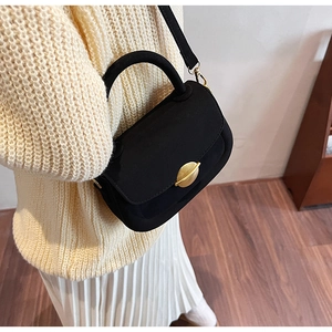 Top view of a black suede saddle bag with gold metal buckle on a beige knit sweater