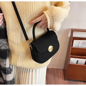 Close-up of black suede semi-circular shoulder bag with a gold circular lock on knit sweater