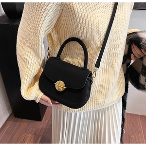 Close-up of a black matte saddle bag with gold metal clasp on a model in knitwear