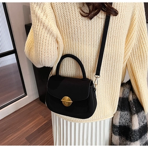 Detail of black suede saddle bag featuring a round gold buckle and versatile straps