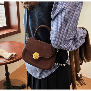 Close-up of vintage brown suede handbag with a gold round clasp shown in a lifestyle setting