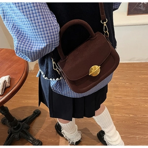 Detail of vintage dark brown suede saddle bag with a round golden clasp and handle