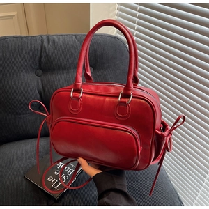 Detalle del bolso Boston rojo en polipiel con bolsillo de cremallera y lazos laterales