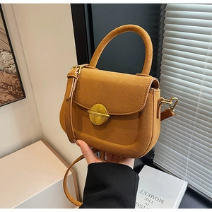Close-up of caramel suede saddle bag with gold magnetic buckle in soft sunlight