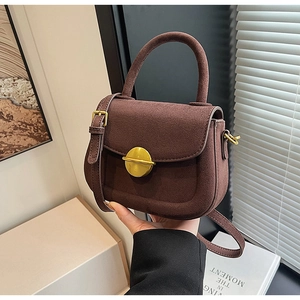 Detail of dark brown suede handbag with large gold round buckle and adjustable strap