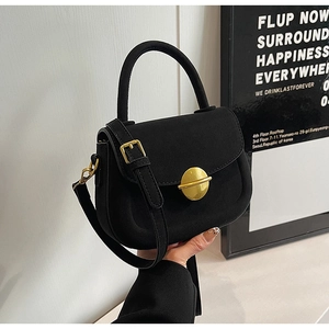Detail of black matte saddle bag showing gold circular buckle and elegant top handle