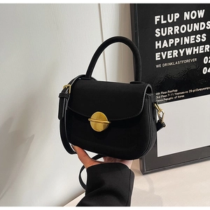 Detail of minimalist black suede handbag with circular gold metal clasp and top handle