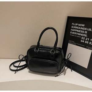 Detalle de un bolso tote de charol negro con bolsillo con cremallera y asas superiores dobles