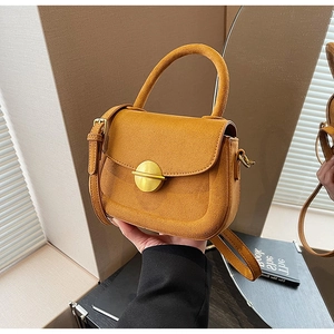 Detail of ginger yellow suede saddle bag with golden metal buckle and top handle
