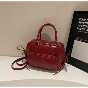 Detalle de un bolso de cuero brillante rojo oscuro con lazos laterales y herrajes plateados