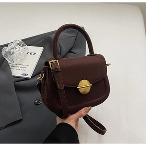 Macro shot of dark brown suede saddle bag with elegant gold round buckle detail