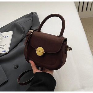 Close-up of matte dark brown saddle bag with vintage gold circular metal buckle detail