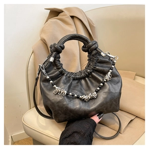 Detail of black pleated cloud bag with pearl chain and silver ring on beige chair
