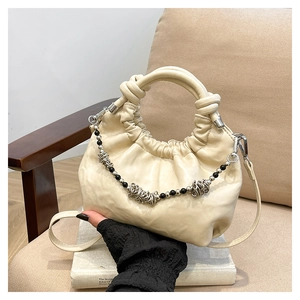 Detail of cream pleated cloud bag featuring decorative bead chain and knotted soft handle