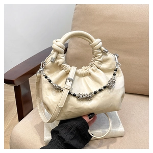 Detail of cream pleated cloud bag with metallic decorative chain on a beige chair