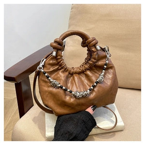 Detailed shot of brown pleated cloud bag with beaded metal chain on beige chair