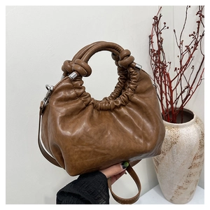 Macro detail of brown leather cloud bag featuring pleated design and knotted handle decoration