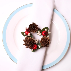 Christmas pine cone napkin ring with red berries and green leaves on white napkin
