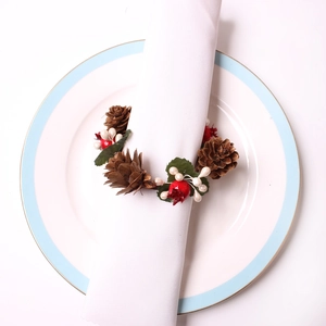 Christmas napkin ring with natural pine cone and red berries on a white plate