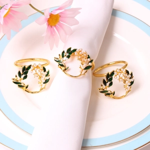 Set di 3 portatovaglioli dorati con foglie verdi e perle su tovagliolo bianco