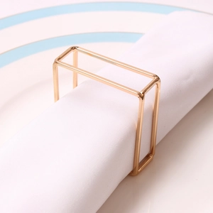 Modern gold rectangular geometric napkin ring displayed on a white cloth on a ceramic plate