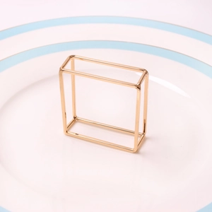 Close-up of a polished gold-plated rectangular geometric napkin ring on a white plate