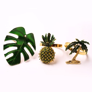 Macro detail of gold tropical napkin rings with pineapple, monstera leaf and palm tree designs