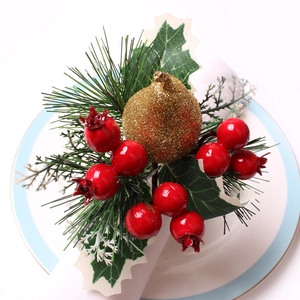 Servilletero navideño con bayas rojas, piñas doradas y agujas de pino verde en un plato