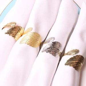 Elegantes servilleteros de pluma en oro y plata sobre servilletas blancas de comedor