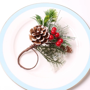 Christmas napkin ring with frosted pine cone, red berries, and green pine needles on white plate