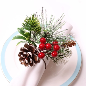 Close-up of pine cone napkin ring with red berries and snow-effect greenery on a plate