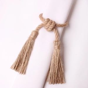 Handcrafted natural jute rope napkin ring featuring a woven knot and twin tassels on white fabric