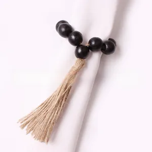 Detail of a black wooden bead napkin ring featuring a natural jute tassel on white cloth