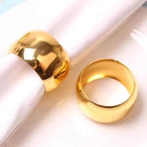 Polished gold drum-shaped metal napkin rings on white ceramic plate and linen cloth
