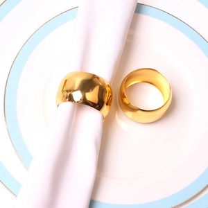 Polished golden drum-shaped metal napkin rings set on white ceramic plates