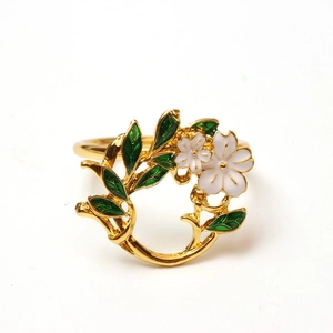 Detailed close-up of golden floral napkin ring with white petals and green enamel leaves