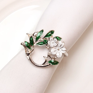 Detail of silver napkin ring with white flowers and green enamel leaves on white linen