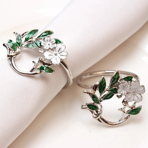 Detail of silver metal gardenia napkin ring with white enamel flower and green leaves
