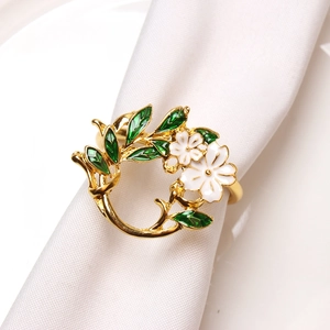Detailed view of floral napkin ring with white enamel flowers and green leaves on gold band