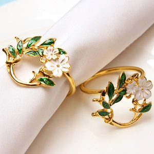 Golden gardenia napkin ring with white enamel flowers and green leaves on white linen